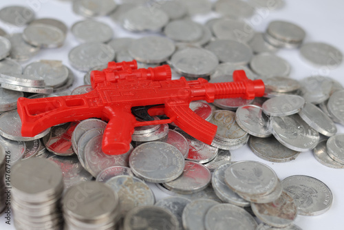 Rupiah money, exchange coin, white coins of different denomination in random order and there red toy gun on top.