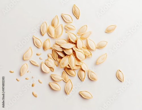 A cluster of light beige pumpkin seeds, scattered on a white surface.  Close-up view of the edible seeds