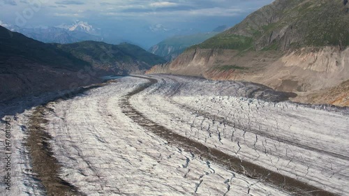 Aerial drone view of stunning view of the Aletsch Glacier in the Swiss Alps, showcasing the immense ice flow surrounded by towering mountains under a clear blue sky. Highlights nature's grandeur.