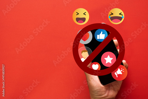 Concept of no social media interaction,Social Media Detox,Social Detoxification.,Hand holding a smartphone with crossed-out among  social media notifications and emoji icons on red background.