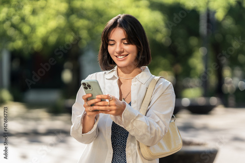A summer day out. A smiling woman checking an app on her phone in the city. Browsing online shops, chatting with friends and family or checking the map for navigation