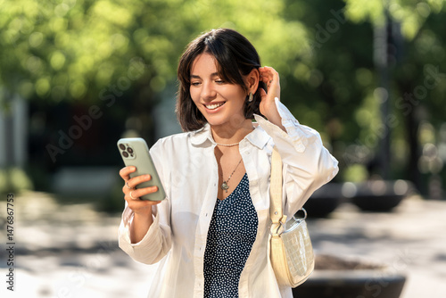 Weekend away. Smiling woman with short trendy hairstyle checking an app on her phone in the city. Browsing online shops, chatting with friends and family or checking the map for directions
