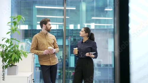 Two colleagues engaged in friendly conversation with coffee in modern office setting. Co-workers, a man and a woman have a friendly conversation. Teamwork, effective communication and collaboration