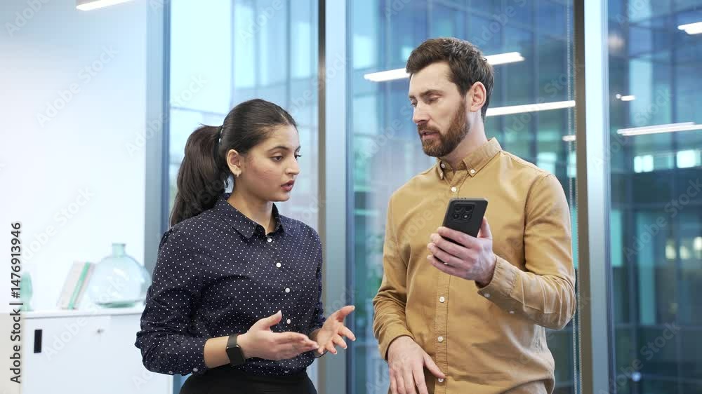 Businessman explains to a female colleague how to use a new application on a mobile phone, talks and teaches. Two coworkers, a man and a woman in office discussing mobile app usage with smartphone