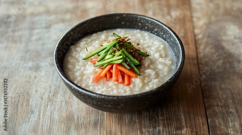Korean cold rice porridge Juk served pickled vegetables normal view of warm rice porridge with soft textured grains garnished with pickled vegetables against a simple wooden surface photo