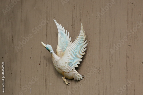 Metal Figurine of a flying Duck attached to brown wooden wall.