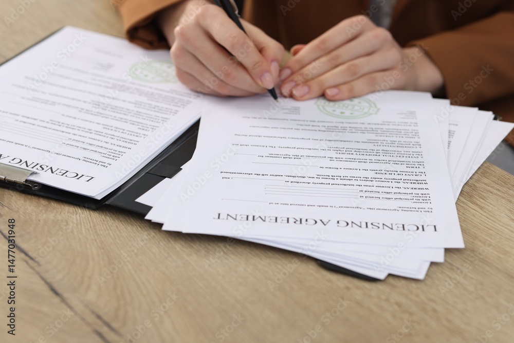 Obraz premium Woman signing licensing agreement document at wooden table indoors, closeup