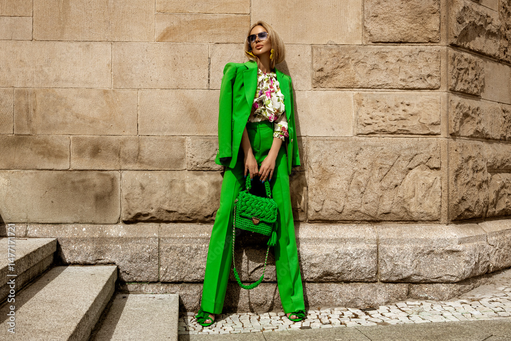 Φωτογραφία Elegant female model in green vibrant suit and fashionable handbag sensually walks in the city on a sunny summer day