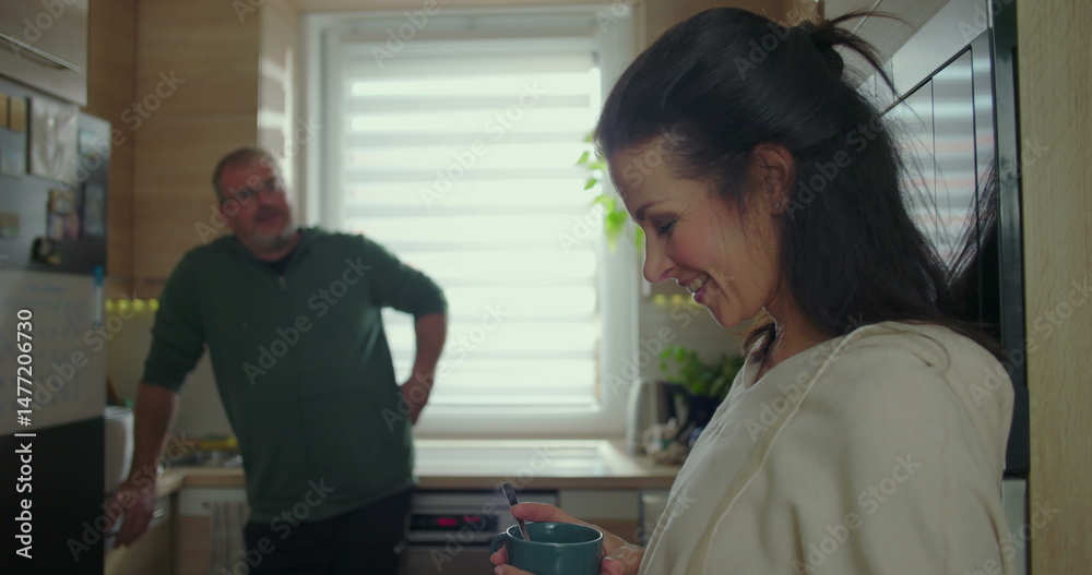 Obraz premium Woman holding a blue mug, casually talking to a man in a modern kitchen, engaging in a warm conversation, relaxed and friendly interaction in a home setting