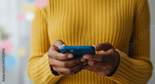 Black woman in yellow sweater using a blue smartphone, blurred background