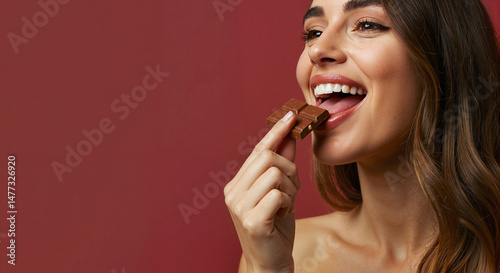 Young woman licking chocolate with a joyful expression against a red background  