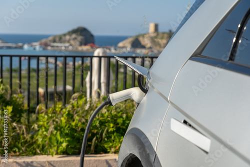 An electric car plugged in a charger agains a bavkground of coastal vacation town