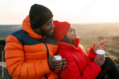 Couple enjoying coffee outdoors in warm jackets during sunset on a scenic hilltop