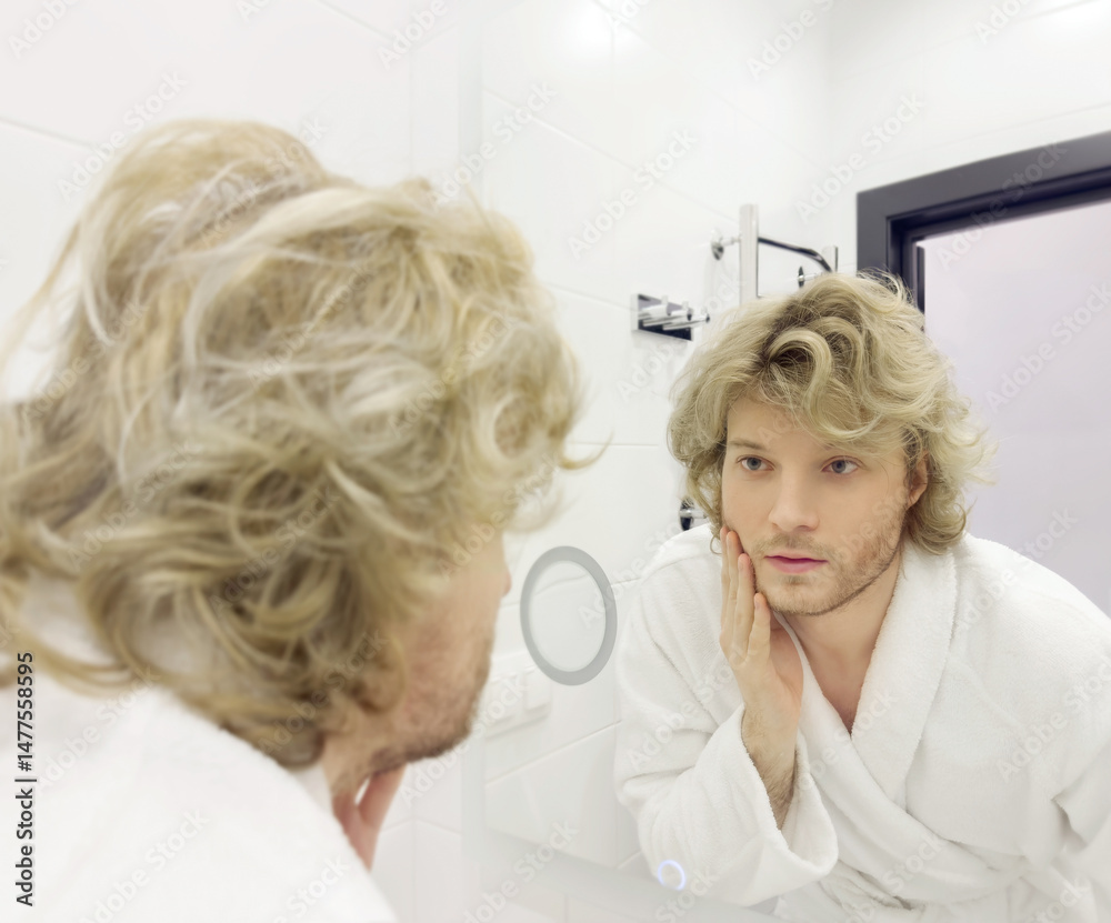Fototapeta premium morning routine, young man looking in mirror in bathroom
