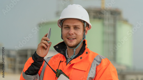 caucasian white engineers in safety uniforms and helmets using laptop and radio for site communication. Concept of teamwork, inspection, and operations at an industrial facility.Construction of Oil, 