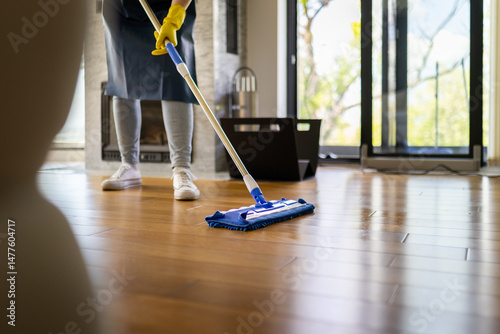 Canvastavla Person cleaning wooden floor with mop in bright living room during daytime