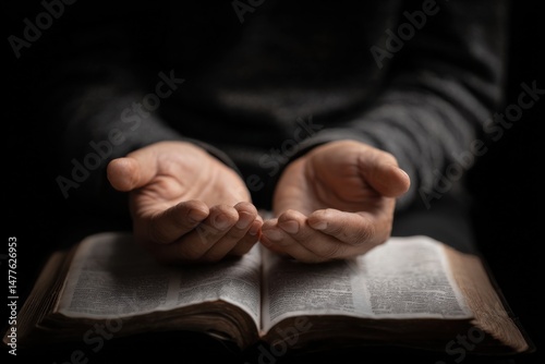 A close-up, intimate shot of a pair of hands gently open and lifted in a posture of prayer above an open resting on the lap.