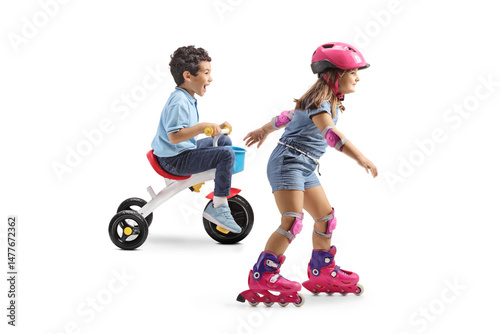 Boy on a trycicle and girl riding rollerblades with helmet, knee and elbow pads