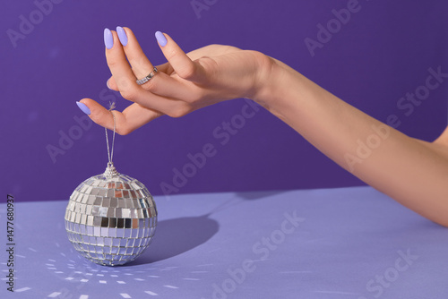 Manicured womans hands holding disco ball on violet background. Manicure, pedicure beauty salon concept