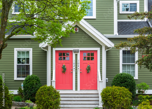 Symmetrical green duplex with coral twin doors framed by spring greenery in Brighton, Massachusetts, USA 
