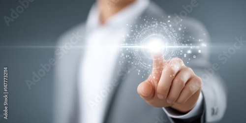 Closeup of a person's hand in a grey suit, index finger touching a glowing orb of light particles against a grey background.