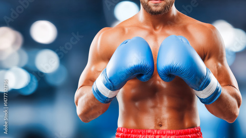 Athletic male boxer with blue boxing gloves and red shorts in fighting stance. Muscular torso and trained physique ready for competition. Powerful fighter prepared for match with professional