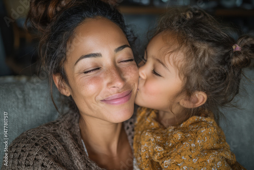 A young daughter lovingly kissing her mother on the cheek while sitting together on the sofa at home, highlighting family affection and care