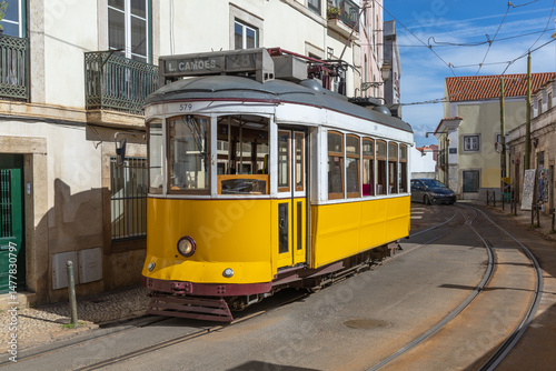 A classic yellow Tram 28 navigates the charming, narrow streets of Lisbon, Portugal on a sunny day.