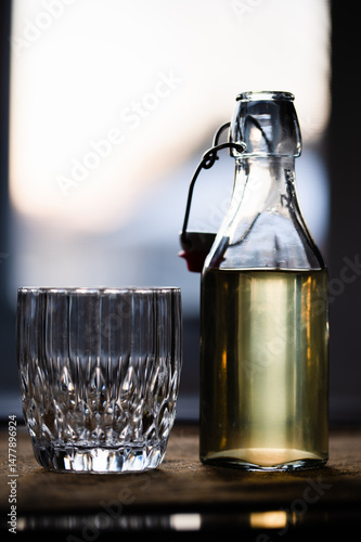 An empty rocks glass on a table next to a flip-top bottle of mead