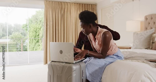 Young couple using laptop on suitcase in cozy bedroom, planning travel adventure