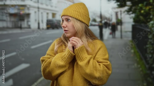 Woman in yellow sweater and hat looks anxious on city street, capturing emotion of fear in urban setting with soft focus background depicting outdoor environment.