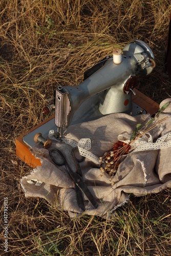 top view sewing machine on a background of dry grass with an old pair of scissors and a linen thread