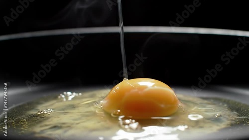 Closeup of egg breaking and frying in pan with rising steam