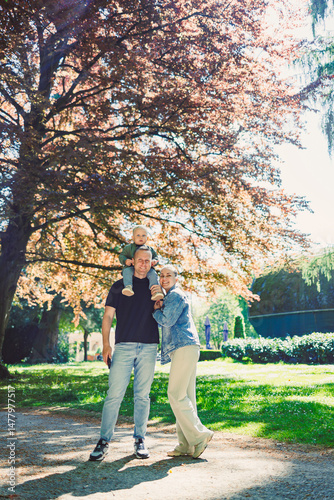 Obraz na płótnie A Truly Joyful Family Moment Captured Underneath a Beautiful Tree in a Sunlit Park Where a Little Child Is Happily Enjoying Being on Their Parents Shoulders, Filling Hearts with Love and Happiness w salonie