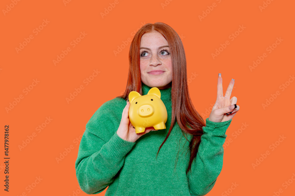 Bright orange backdrop highlights a young woman holding a yellow piggy bank while flashing a peace sign, representing financial savings and positivity Bright orange backdrop highlights a young woman holding a yellow piggy bank while flashing a peace sign, representing financial savings and positivity