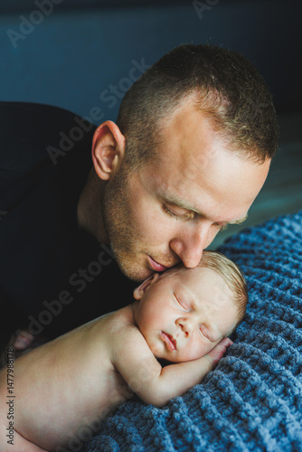 Obraz na płótnie In a serene and peaceful atmosphere, a father gently kisses his precious newborn, illustrating the profound emotional bond and unconditional love that beautifully define the essence of fatherhood w salonie