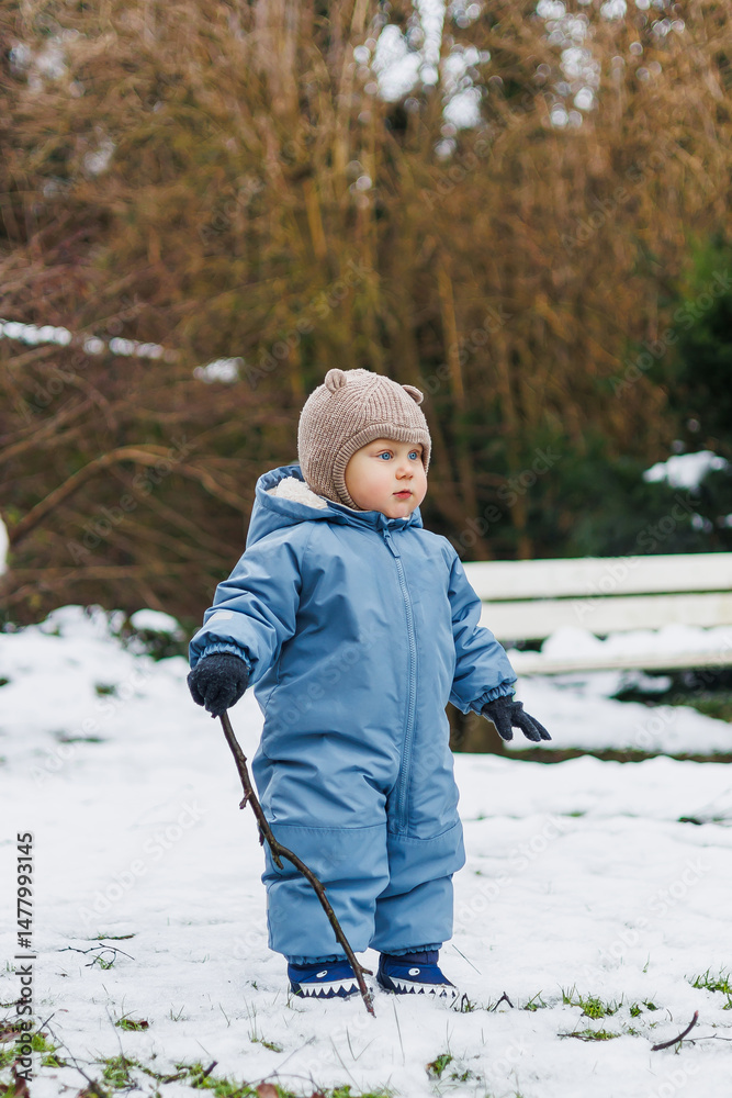 A Joyful Child Playing in a Winter Wonderland Dressed in a Cozy Blue Snowsuit and HandKnit Hat, This Little One Explores Nature in the Snowy Landscape, Experiencing Pure Happiness