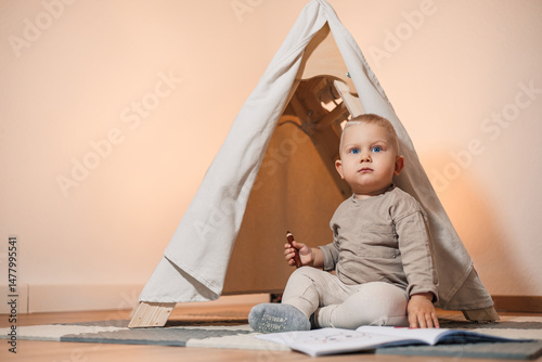 Obraz na płótnie An Adorable Toddler Enjoys Playing Inside a Cozy Indoor Tent Surrounded by Soft Cushions While Reading a Colorful Book, Imbuing a Sense of Adventure and Imagination in a Warm Home Environment w salonie