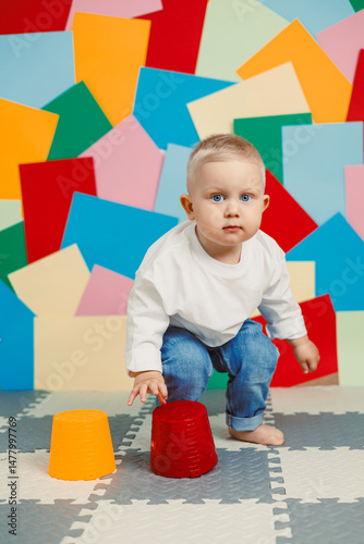 An adorable, energetic toddler is actively playing with an assortment of colorful cups set against a vibrant and fun background, showcasing the joys of childhood exploration and creativity
