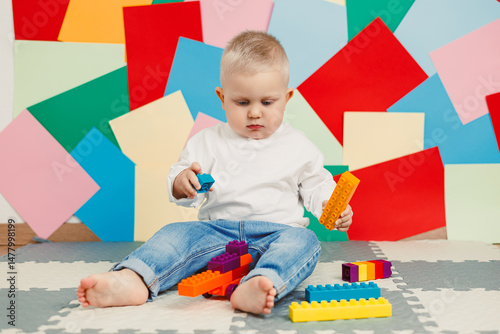 Obraz na płótnie In a bright playroom full of toys, a cheerful toddler joyfully builds with colorful blocks, creating a fun and stimulating environment ideal for exploration and learning through play w salonie