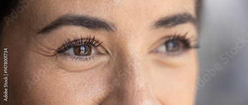 Looking far away. Cropped close up pretty smiling young female with dark eyes look aside. Selective focus on one eye. Good vision after laser correction surgery contact lens concept. Panoramic photo