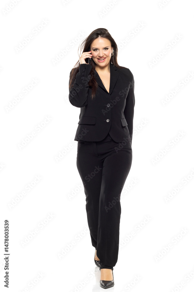 Smiling business woman walking in the white studio and talking on mobile phone Smiling business woman walking in the white studio and talking on mobile phone
