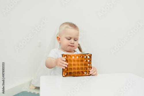 Obraz na płótnie A curious and adorable toddler is examining a delicious waffle in a bright and minimalist setting, showcasing an engaging moment filled with joy, imagination, and exploration during mealtime w salonie