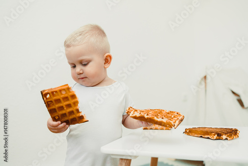 A delightful and cute child is excitedly exploring the delicious waffles in front of them, filled with curiosity and joy, all while situated in a bright and minimalist kitchen setting