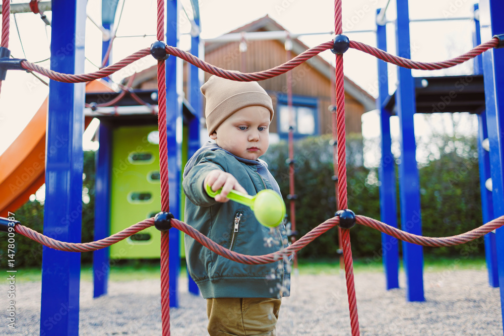An adorable toddler joyfully playing at an outdoor playground surrounded by a colorful climbing structure and a fun slide, creating a vibrant atmosphere and fostering happy childhood memories