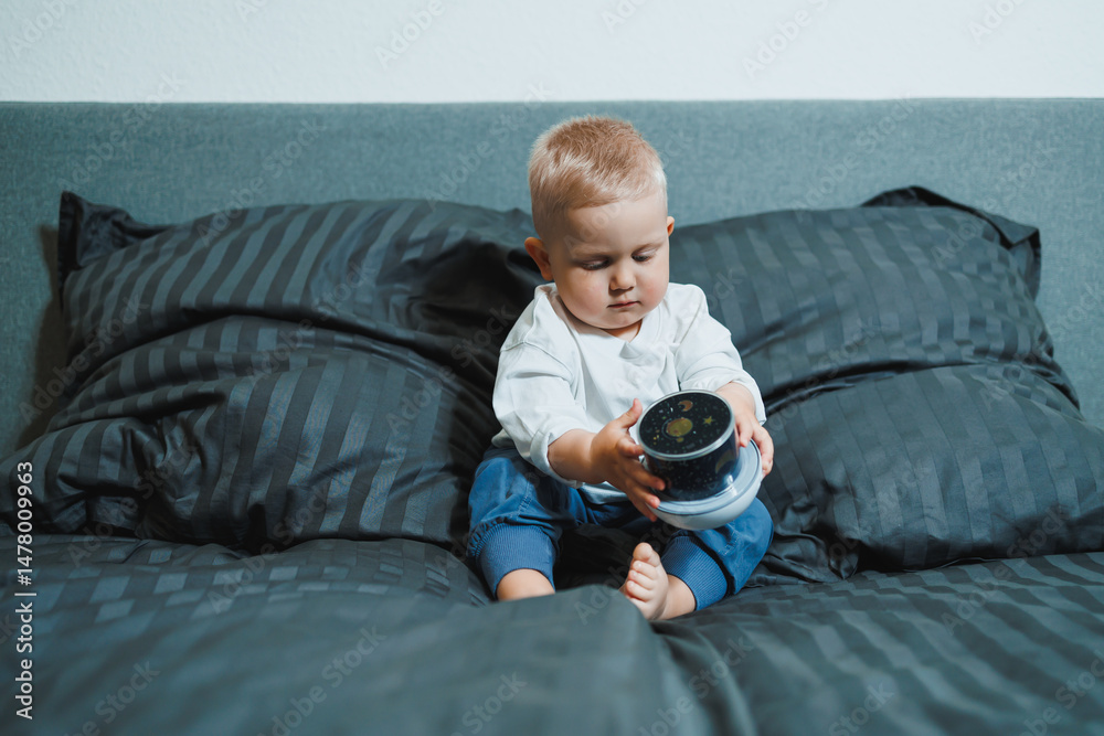 A joyful and happy toddler is happily and energetically playing with a colorful container on a cozy, warm bed surrounded by soft, fluffy pillows, showcasing the pure joy and wonder of early childhood