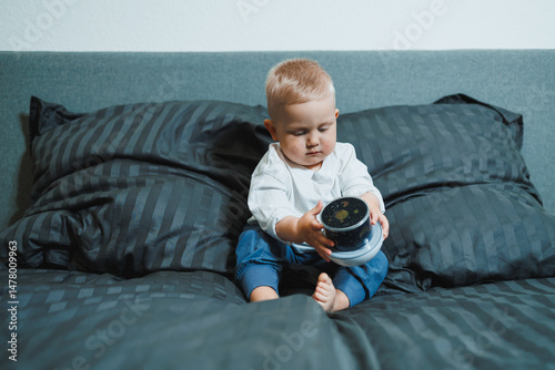 Obraz na płótnie A joyful and happy toddler is happily and energetically playing with a colorful container on a cozy, warm bed surrounded by soft, fluffy pillows, showcasing the pure joy and wonder of early childhood w salonie