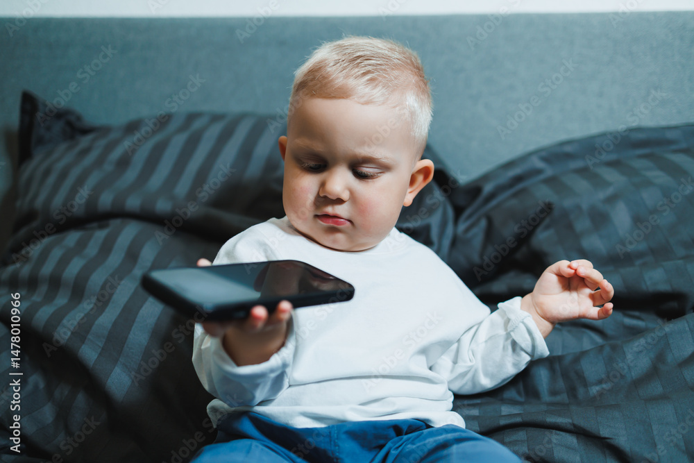 A curious toddler is happily engaged with a smartphone while comfortably nestled in a cozy bed surrounded by soft cushions, embodying the innocence and carefree spirit of childhood and playtime