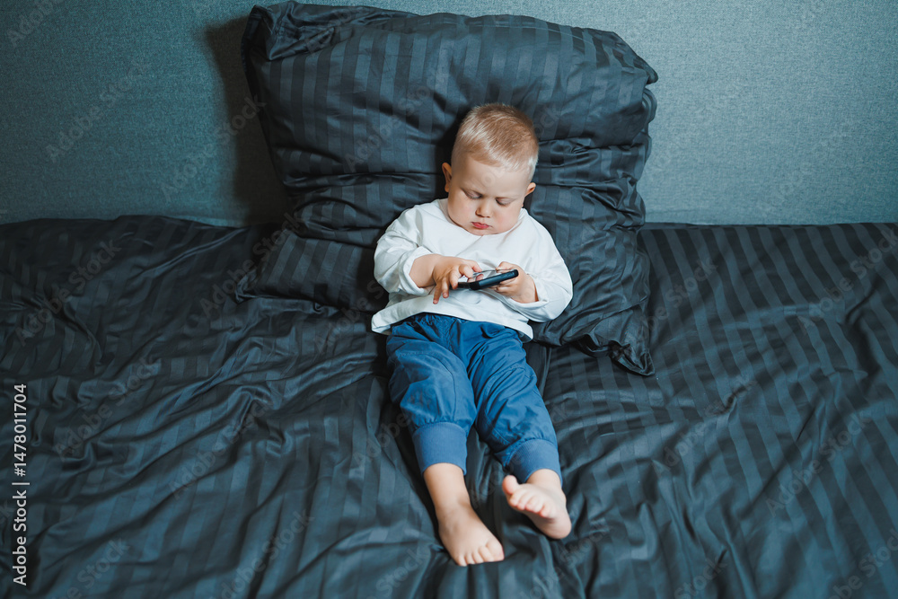 A young child can be seen fully engaged with a mobile device while comfortably relaxing on their bed, creating a delightful scene that captures the innocence and curiosity of childhood