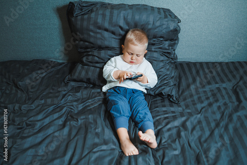 Obraz na płótnie A young child can be seen fully engaged with a mobile device while comfortably relaxing on their bed, creating a delightful scene that captures the innocence and curiosity of childhood w salonie